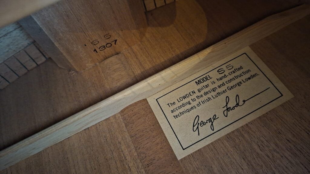 Ein Blick auf das Innere der Lowden S-5 Akustik Gitarre zeigt ein vom Gitarrenbauer George Lowden signiertes Etikett, das die handgefertigte Konstruktion und die einzigartigen Designtechniken hervorhebt. Ein Blick auf das Innere der Lowden S-5 Akustik Gitarre zeigt ein vom Gitarrenbauer George Lowden signiertes Etikett, das die handgefertigte Konstruktion und die einzigartigen Designtechniken hervorhebt.