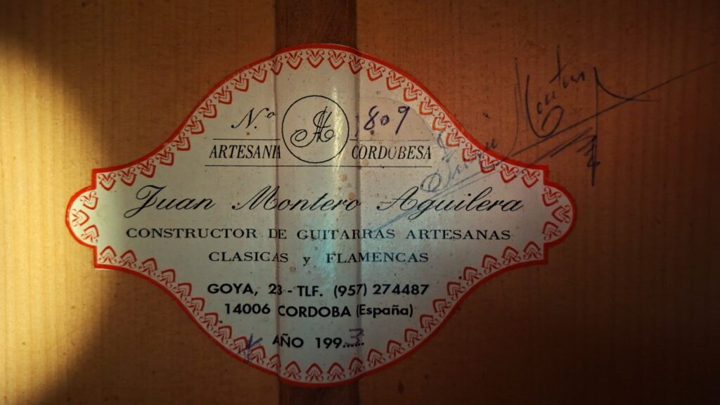 Eine Nahaufnahme zeigt das Etikett einer Juan Montero 1993 Blanca Flamenco Gitarre mit der Aufschrift "Juan Montero Aguilera, Constructor de Guitarras Artesanas Clasicas y Flamencas, Córdoba, España" und einer Unterschrift daneben. Eine Nahaufnahme zeigt das Etikett einer Juan Montero 1993 Blanca Flamenco Gitarre mit der Aufschrift "Juan Montero Aguilera, Constructor de Guitarras Artesanas Clasicas y Flamencas, Córdoba, España" und einer Unterschrift daneben.
