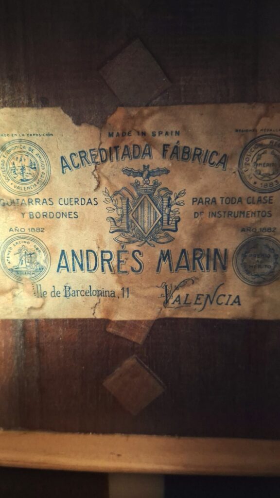 Ein altes, vergilbtes Etikett im Inneren der Andres Marin 1890 Klassische Gitarre lautet: "Acreditada Fábrica Andrés Marín, Valencia", mit verschnörkelten Rändern und einem Wappen, das für Streichinstrumente wirbt und eine Adresse in Barcelona, Spanien, angibt. Ein altes, vergilbtes Etikett im Inneren der Andres Marin 1890 Klassische Gitarre lautet: "Acreditada Fábrica Andrés Marín, Valencia", mit verschnörkelten Rändern und einem Wappen, das für Streichinstrumente wirbt und eine Adresse in Barcelona, Spanien, angibt.