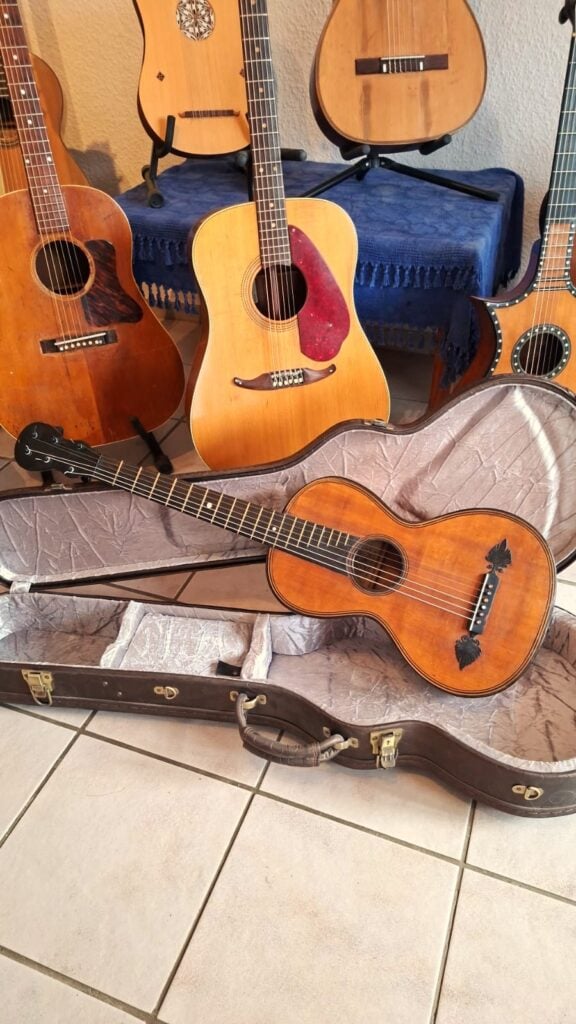 Im Hintergrund stehen mehrere Akustikgitarren aufrecht, während eine Stephan-Thumhart-Romantikgitarre von 1838 in einem offenen, mit Samt ausgekleideten Koffer auf dem Fliesenboden liegt. Die Szene spielt sich in einem Innenraum ab. Im Hintergrund stehen mehrere Akustikgitarren aufrecht, während eine Stephan-Thumhart-Romantikgitarre von 1838 in einem offenen, mit Samt ausgekleideten Koffer auf dem Fliesenboden liegt. Die Szene spielt sich in einem Innenraum ab.