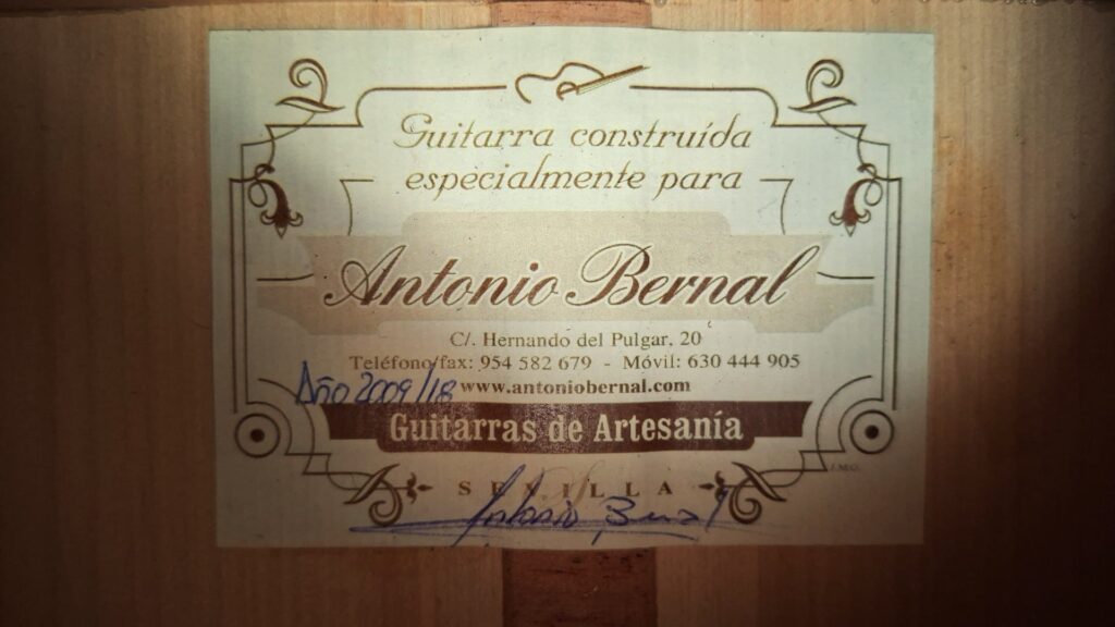 Eine Nahaufnahme zeigt das Etikett im Inneren der Antonio-Bernal-Flamenco-Gitarre aus dem Jahr 2009 mit der Aufschrift „Guitarra construida especialmente para Antonio Bernal“ sowie Kontaktdaten, Website, handschriftliche Unterschrift und die Seriennummer der Gitarre. Eine Nahaufnahme zeigt das Etikett im Inneren der Antonio-Bernal-Flamenco-Gitarre aus dem Jahr 2009 mit der Aufschrift „Guitarra construida especialmente para Antonio Bernal“ sowie Kontaktdaten, Website, handschriftliche Unterschrift und die Seriennummer der Gitarre.