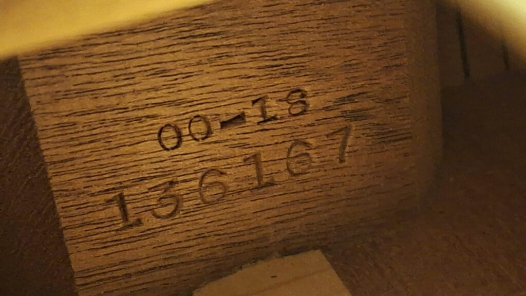 Nahaufnahme der auf die Holzinnenseite einer Martin 00-18 Akustikgitarre aus dem Jahr 1954 eingeprägten Zahlen und Buchstaben, die die Aufschrift „00-18“ oberhalb der Seriennummer „136167“ zeigt. Nahaufnahme der auf die Holzinnenseite einer Martin 00-18 Akustikgitarre aus dem Jahr 1954 eingeprägten Zahlen und Buchstaben, die die Aufschrift „00-18“ oberhalb der Seriennummer „136167“ zeigt.