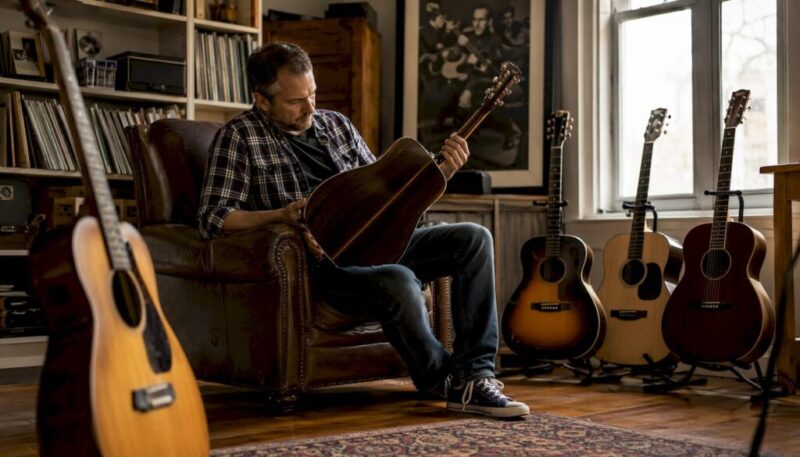 Man examining acoustic guitar body shapes in studio