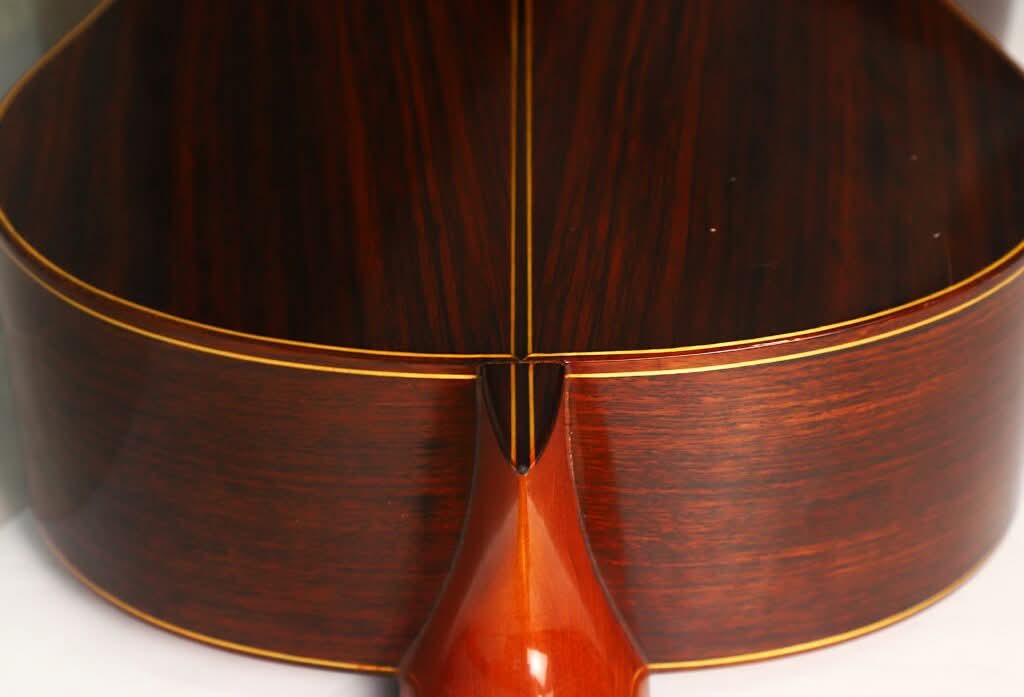 Nahaufnahme des Bodens und der Zargen der „Antonio Duran 1974 Klassische Gitarre“, gefertigt aus dunklem, poliertem Holz mit gelblicher Einfassung, die den Übergang zwischen Hals und Korpus hervorhebt. Nahaufnahme des Bodens und der Zargen der „Antonio Duran 1974 Klassische Gitarre“, gefertigt aus dunklem, poliertem Holz mit gelblicher Einfassung, die den Übergang zwischen Hals und Korpus hervorhebt.