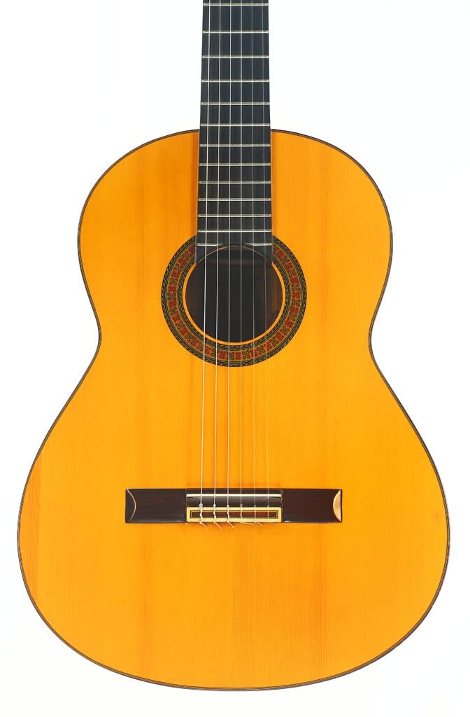 Die „Sobrinos de Santos Hernandez 1974 Flamenco-Gitarre“ ist eine sechssaitige Akustikgitarre mit naturbelassener Holzoberfläche, rundem Schallloch mit dekorativer Rosette und dunklem Griffbrett, die vor einem weißen Hintergrund abgebildet ist. Die „Sobrinos de Santos Hernandez 1974 Flamenco-Gitarre“ ist eine sechssaitige Akustikgitarre mit naturbelassener Holzoberfläche, rundem Schallloch mit dekorativer Rosette und dunklem Griffbrett, die vor einem weißen Hintergrund abgebildet ist.