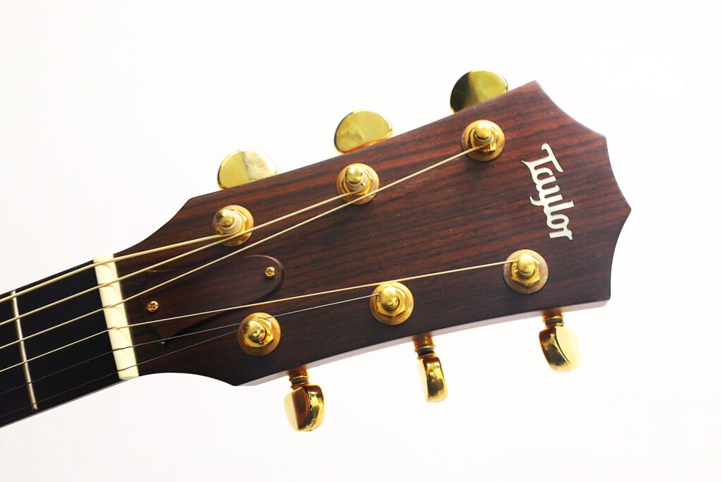 Nahaufnahme des Kopfes einer Taylor 712 Akustikgitarre mit goldenen Stimmwirbeln vor weißem Hintergrund. Nahaufnahme des Kopfes einer Taylor 712 Akustikgitarre mit goldenen Stimmwirbeln vor weißem Hintergrund.