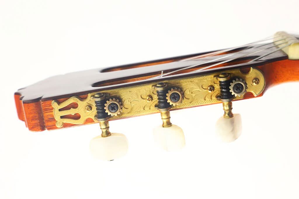 Nahaufnahme des Kopfstücks einer „Klassische Gitarre“ von Antonio Duran aus dem Jahr 1974 mit drei Stimmwirbeln, goldenen Zahnrädern und einem Teil des Holzhalses vor weißem Hintergrund. Nahaufnahme des Kopfstücks einer „Klassische Gitarre“ von Antonio Duran aus dem Jahr 1974 mit drei Stimmwirbeln, goldenen Zahnrädern und einem Teil des Holzhalses vor weißem Hintergrund.