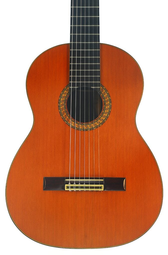 Eine klassische Gitarre vom Typ „Melchor Rodriguez 1980 Ramirez Stil“ mit einem Korpus aus Holz, sieben Saiten und einer dekorativen Rosette um das Schallloch, präsentiert vor einem weißen Hintergrund. Eine klassische Gitarre vom Typ „Melchor Rodriguez 1980 Ramirez Stil“ mit einem Korpus aus Holz, sieben Saiten und einer dekorativen Rosette um das Schallloch, präsentiert vor einem weißen Hintergrund.