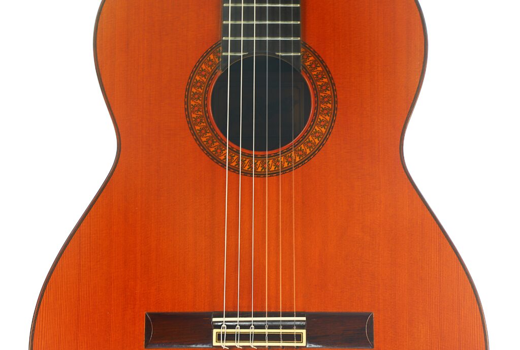 Nahaufnahme des Korpus einer José Ramirez 1a 1973 Klassische Gitarre, die sechs Saiten, das Schallloch mit dekorativer Rosette und einen Teil des Griffbretts vor weißem Hintergrund zeigt. Nahaufnahme des Korpus einer José Ramirez 1a 1973 Klassische Gitarre, die sechs Saiten, das Schallloch mit dekorativer Rosette und einen Teil des Griffbretts vor weißem Hintergrund zeigt.