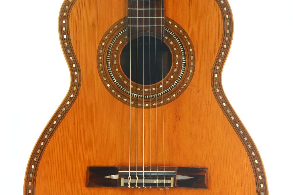 Nahaufnahme der Vorderseite der „Salvador Ibanez 1900 Klassische Gitarre“, die das Schallloch mit dekorativer Einlage, die Saiten und einen Teil des Stegs vor weißem Hintergrund zeigt. Nahaufnahme der Vorderseite der „Salvador Ibanez 1900 Klassische Gitarre“, die das Schallloch mit dekorativer Einlage, die Saiten und einen Teil des Stegs vor weißem Hintergrund zeigt.