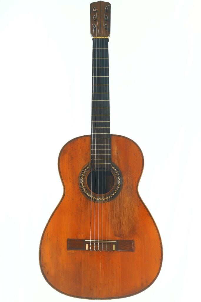 Eine klassischeaRicardo Sanchis Nacher 1940 Augustin Barrios Klassische Gitarre – Eine spanische Meistergitarre mit der Seele der großen Konzertbühnen Gitarre von Ricardo Sanchis Nacher aus dem Jahr 1940 nach dem Vorbild von Agustín Barrios mit einem Korpus aus Holz, sechs Saiten und einem dunklen Griffbrett, fotografiert vor einem schlichten weißen Hintergrund. Ricardo Sanchis Nacher 1940 Augustin Barrios Klassische Gitarre – Eine spanische Meistergitarre mit der Seele der großen Konzertbühnen