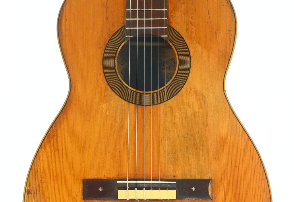 Nahaufnahme des Korpus einer „José Ramirez 1932 Klassische Gitarre“ mit sechs Saiten, einem Steg aus Holz und dem Schallloch mit Zierringen. Nahaufnahme des Korpus einer „José Ramirez 1932 Klassische Gitarre“ mit sechs Saiten, einem Steg aus Holz und dem Schallloch mit Zierringen.