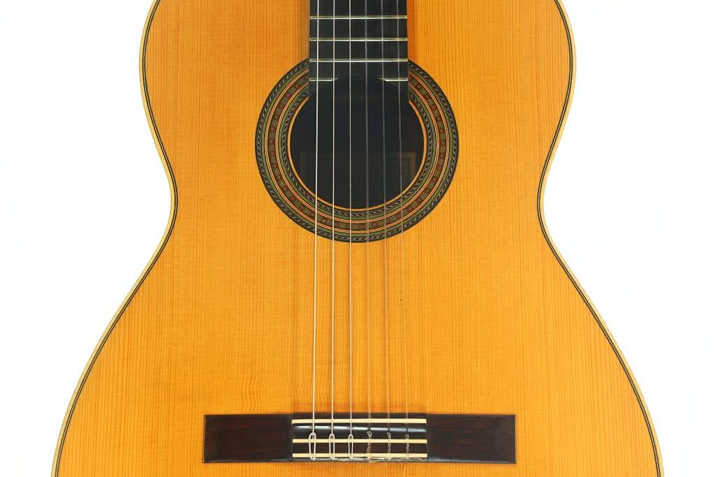Nahaufnahme der Alastair McNeil 1997 Hauser Klassische Gitarre, die ihren Korpus im Stil einer klassischen Akustikgitarre mit sechs Saiten, einer detailreichen Schalllochrosette und einem Steg aus Holz vor weißem Hintergrund zeigt. Nahaufnahme der Alastair McNeil 1997 Hauser Klassische Gitarre, die ihren Korpus im Stil einer klassischen Akustikgitarre mit sechs Saiten, einer detailreichen Schalllochrosette und einem Steg aus Holz vor weißem Hintergrund zeigt.