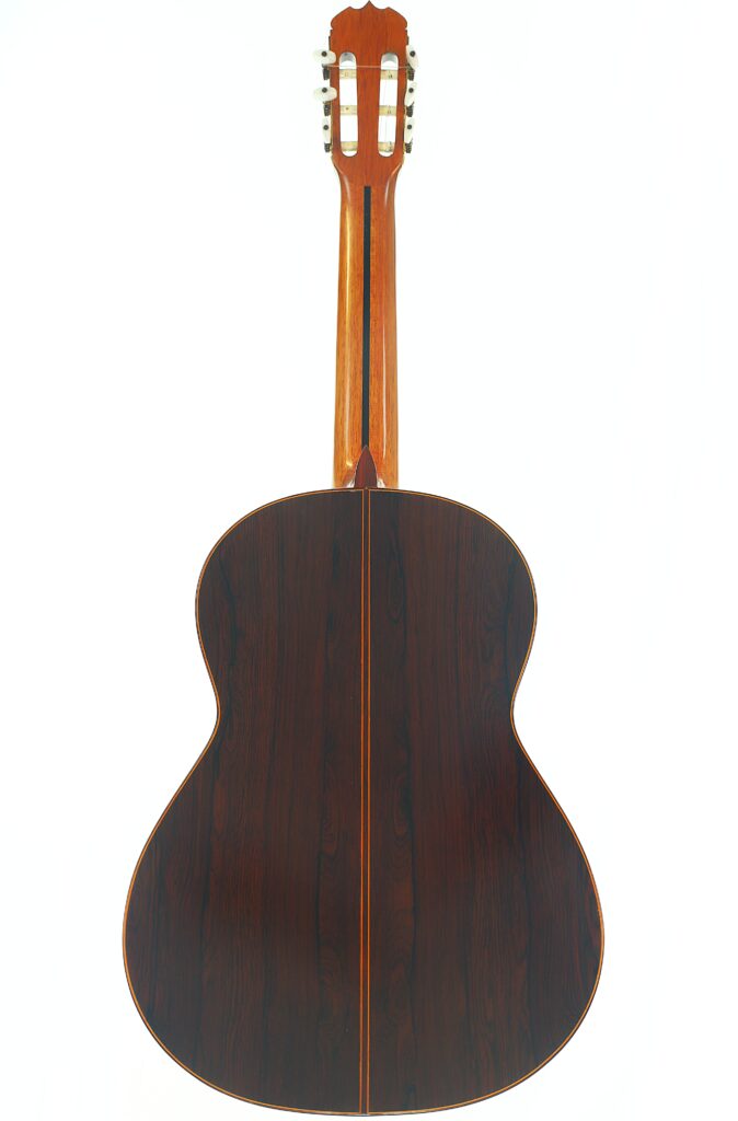 Die Rückansicht einer José Ramirez 1a 1973 Klassische Gitarre zeigt eine klassische Akustikgitarre mit dunkler Holzoberfläche, hervorstechenden Maserungen und einer markanten Mittelnaht, die in der Mitte verläuft. Die Rückansicht einer José Ramirez 1a 1973 Klassische Gitarre zeigt eine klassische Akustikgitarre mit dunkler Holzoberfläche, hervorstechenden Maserungen und einer markanten Mittelnaht, die in der Mitte verläuft.