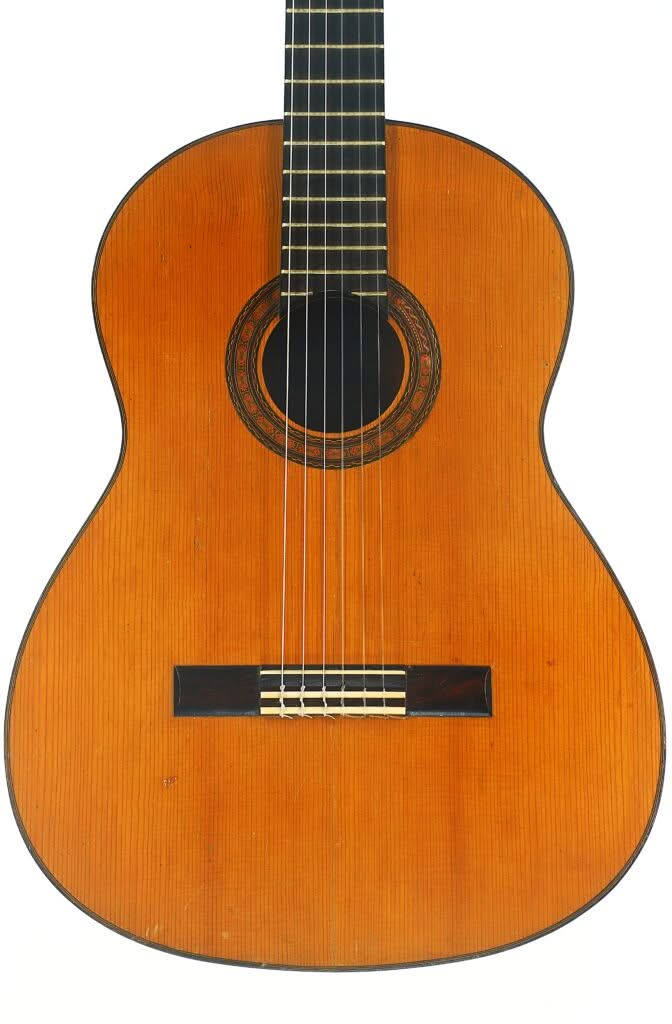 Die Flamenco-Gitarre „Manuel de la Chica 1954“ ist eine klassische Akustikgitarre mit einem Holzkorpus, sechs Saiten, einer dekorativen Rosette um das runde Schallloch und einem dunklen Steg, die vor einem weißen Hintergrund abgebildet ist. Die Flamenco-Gitarre „Manuel de la Chica 1954“ ist eine klassische Akustikgitarre mit einem Holzkorpus, sechs Saiten, einer dekorativen Rosette um das runde Schallloch und einem dunklen Steg, die vor einem weißen Hintergrund abgebildet ist.