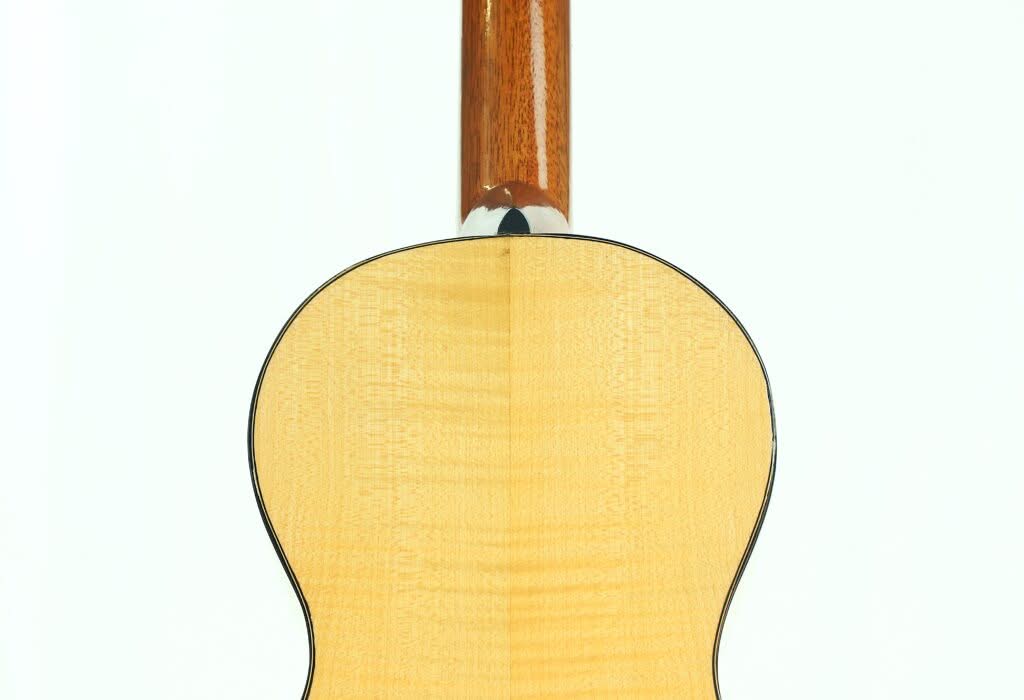 Nahaufnahme des Rückens der Lacote Stil Romantikgitarre mit einem Korpus aus hellem Holz mit glänzender Oberfläche, einem nach oben verlaufenden, dunkleren Holzhals und schwarz umrandeten Kanten. Nahaufnahme des Rückens der Lacote Stil Romantikgitarre mit einem Korpus aus hellem Holz mit glänzender Oberfläche, einem nach oben verlaufenden, dunkleren Holzhals und schwarz umrandeten Kanten.