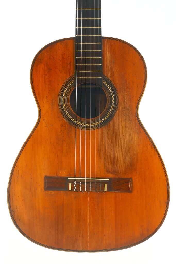 Eine Nahaufnahme der „Ricardo Sanchis Nacher 1940 Augustin Barrios Klassische Gitarre“ vor weißem Hintergrund, die den Holzkorpus, die Saiten und einen Teil des Halses hervorhebt. Die Gitarre verfügt über ein rundes Schallloch mit dekorativer Einlage. Eine Nahaufnahme der „Ricardo Sanchis Nacher 1940 Augustin Barrios Klassische Gitarre“ vor weißem Hintergrund, die den Holzkorpus, die Saiten und einen Teil des Halses hervorhebt. Die Gitarre verfügt über ein rundes Schallloch mit dekorativer Einlage.