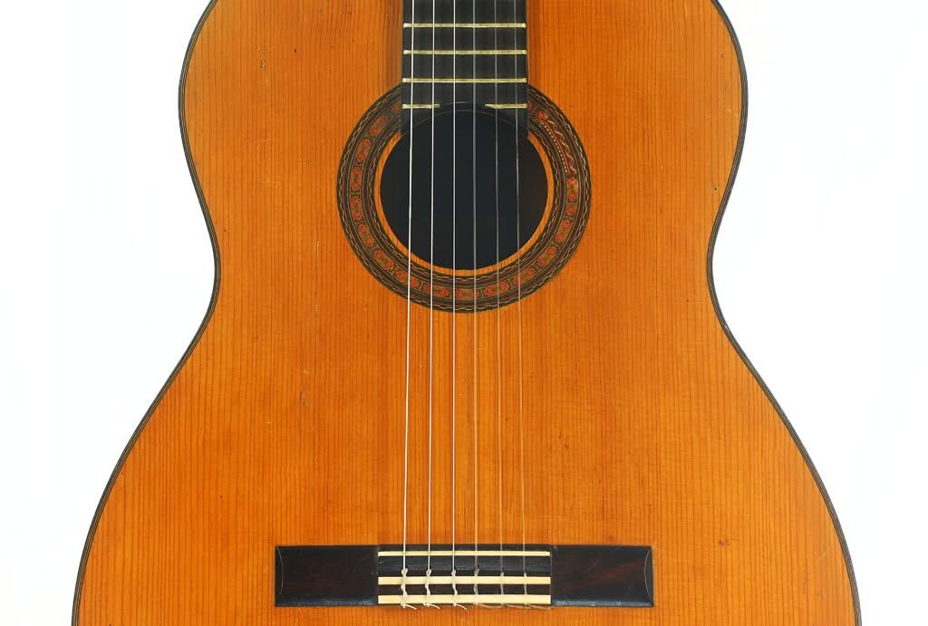 Nahaufnahme des Korpus einer Flamenco-Gitarre von Manuel de la Chica aus dem Jahr 1954 mit sechs Saiten, einem Steg aus Holz und einer dekorativen Rosette um das Schallloch auf weißem Hintergrund. Nahaufnahme des Korpus einer Flamenco-Gitarre von Manuel de la Chica aus dem Jahr 1954 mit sechs Saiten, einem Steg aus Holz und einer dekorativen Rosette um das Schallloch auf weißem Hintergrund.
