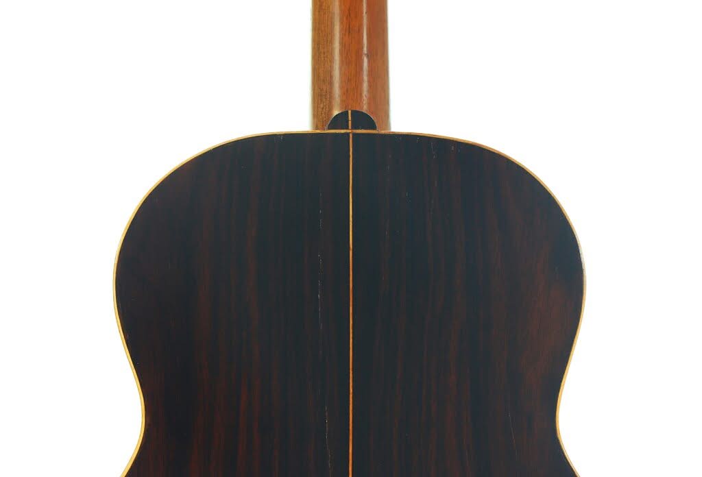 Das Bild zeigt die Rückseite einer „Klassische Gitarre“ von Salvador Ibanez aus dem Jahr 1900, die aus dunklem Holz mit sichtbarer Maserung gefertigt ist und eine mittige Naht sowie helle Kanten aufweist. Der Hals ist oben teilweise zu sehen. Das Bild zeigt die Rückseite einer „Klassische Gitarre“ von Salvador Ibanez aus dem Jahr 1900, die aus dunklem Holz mit sichtbarer Maserung gefertigt ist und eine mittige Naht sowie helle Kanten aufweist. Der Hals ist oben teilweise zu sehen.