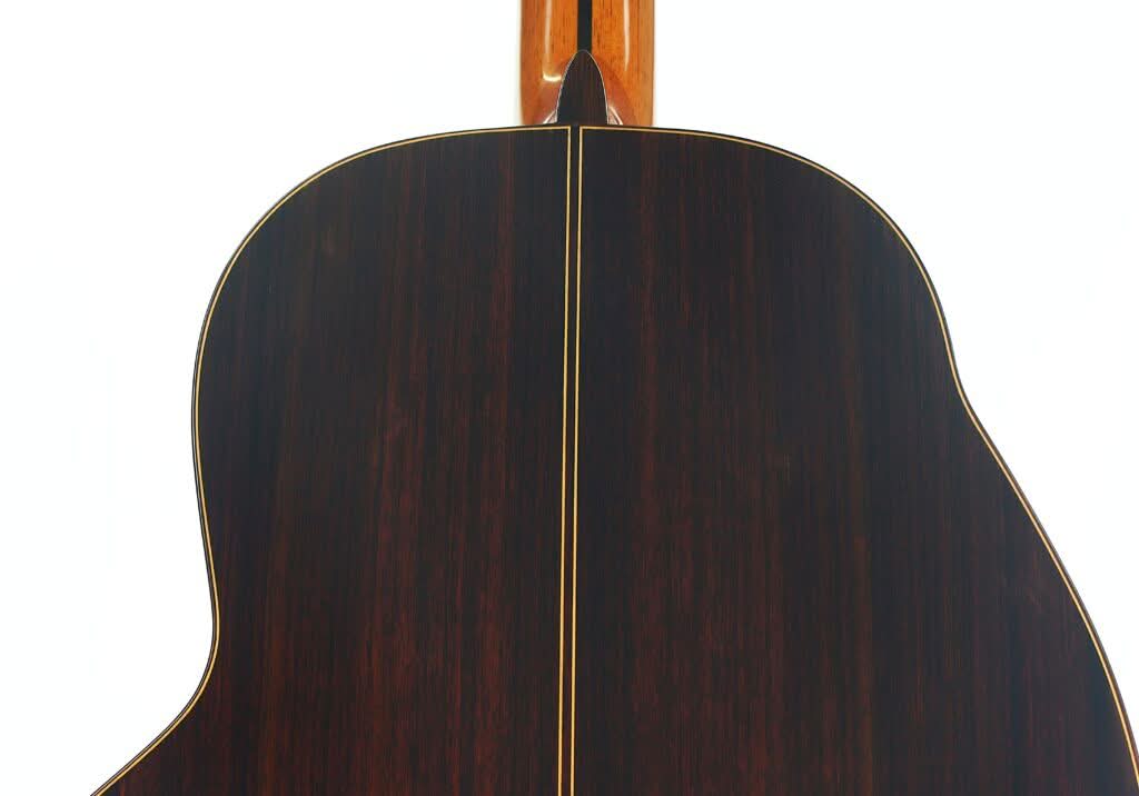 Nahaufnahme der Rückseite der „Gran Klassische Gitarre“ von Raimundo y Aparicio Corujo, gefertigt aus dunklem Holz mit einer hellen Mittelnaht und Einfassung, die die Holzmaserung und die glatte Oberfläche hervorheben. Nahaufnahme der Rückseite der „Gran Klassische Gitarre“ von Raimundo y Aparicio Corujo, gefertigt aus dunklem Holz mit einer hellen Mittelnaht und Einfassung, die die Holzmaserung und die glatte Oberfläche hervorheben.