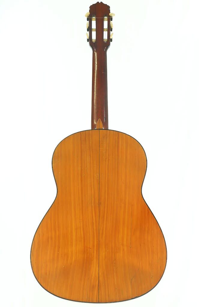 Das Bild zeigt die Rückseite einer Flamenco-Gitarre von Manuel de la Chica aus dem Jahr 1954 mit einem Holzkorpus, der dunkle Kanten und eine sichtbare Maserung aufweist, fotografiert vor einem weißen Hintergrund. Das Bild zeigt die Rückseite einer Flamenco-Gitarre von Manuel de la Chica aus dem Jahr 1954 mit einem Holzkorpus, der dunkle Kanten und eine sichtbare Maserung aufweist, fotografiert vor einem weißen Hintergrund.