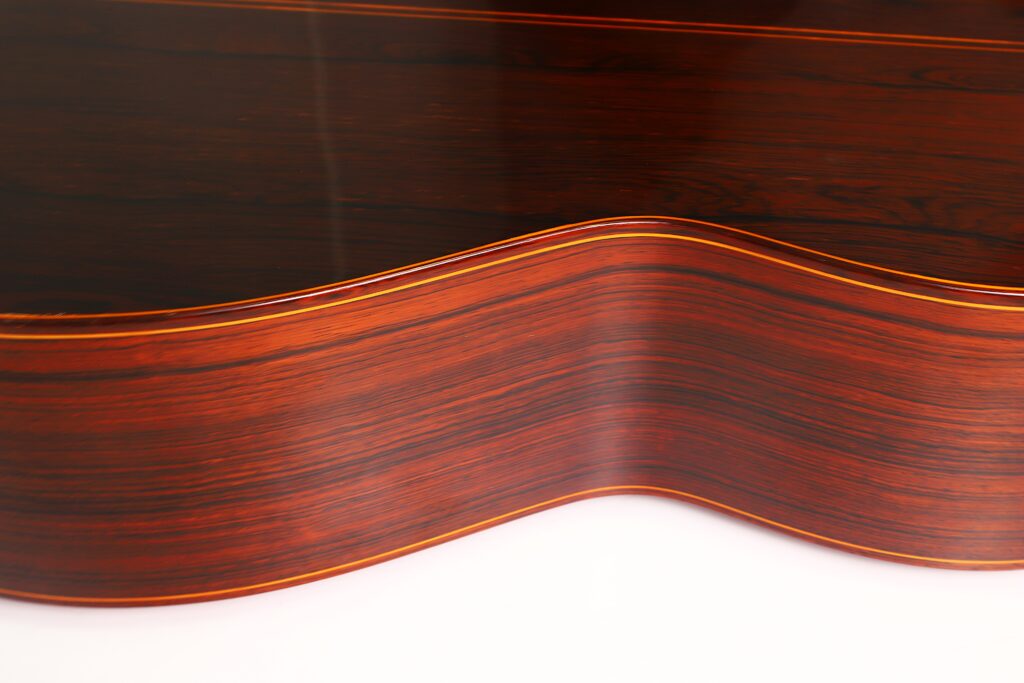 Nahaufnahme der glatten, dunklen Holzseite einer José Ramirez 1a 1973 Klassische Gitarre, die ihre geschwungene Form und die feine Maserung mit glänzender Oberfläche zeigt. Nahaufnahme der glatten, dunklen Holzseite einer José Ramirez 1a 1973 Klassische Gitarre, die ihre geschwungene Form und die feine Maserung mit glänzender Oberfläche zeigt.