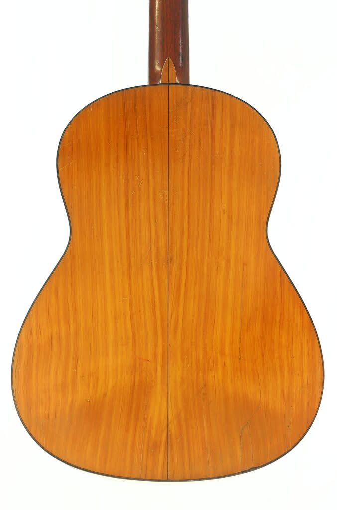 Das Bild zeigt die Rückseite einer Flamenco-Gitarre von Manuel de la Chica aus dem Jahr 1954, die aus glattem, poliertem Holz gefertigt ist und in der Mitte eine vertikale Naht aufweist; sie ist vor einem weißen Hintergrund abgebildet. Das Bild zeigt die Rückseite einer Flamenco-Gitarre von Manuel de la Chica aus dem Jahr 1954, die aus glattem, poliertem Holz gefertigt ist und in der Mitte eine vertikale Naht aufweist; sie ist vor einem weißen Hintergrund abgebildet.