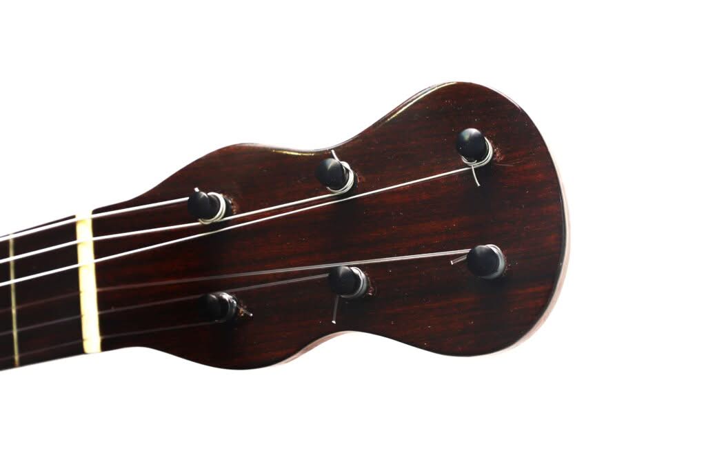 Nahaufnahme des Kopfes einer Lacote Stil Romantikgitarre aus dunklem Holz mit vier Stimmwirbeln und Saiten vor weißem Hintergrund. Nahaufnahme des Kopfes einer Lacote Stil Romantikgitarre aus dunklem Holz mit vier Stimmwirbeln und Saiten vor weißem Hintergrund.