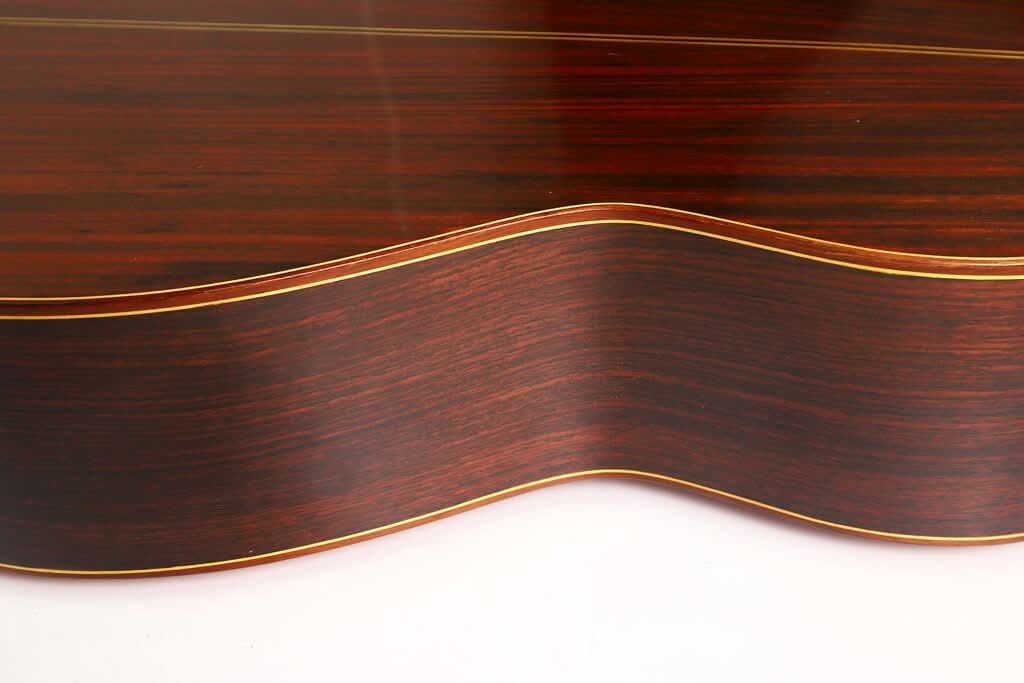 Nahaufnahme der Seite einer „Klassische Gitarre“ von Antonio Duran aus dem Jahr 1974, die die dunkle Holzmaserung, die hellen Zierleisten und die anmutige Wölbung des Korpus vor weißem Hintergrund hervorhebt. Nahaufnahme der Seite einer „Klassische Gitarre“ von Antonio Duran aus dem Jahr 1974, die die dunkle Holzmaserung, die hellen Zierleisten und die anmutige Wölbung des Korpus vor weißem Hintergrund hervorhebt.