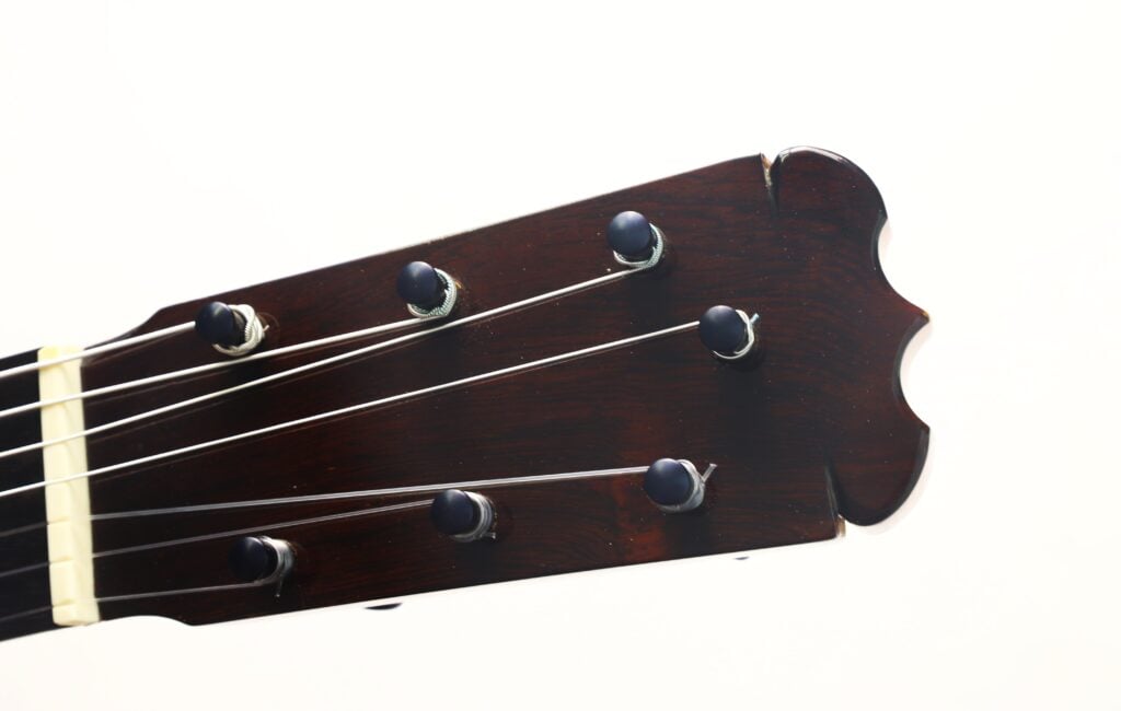 Nahaufnahme des Kopfes einer 7-saitigen klassischen Gitarre vom Typ „Ramirez Stil“ von Melchor Rodriguez aus dem Jahr 1980, auf der sieben Stimmwirbel und Saiten vor weißem Hintergrund zu sehen sind. Nahaufnahme des Kopfes einer 7-saitigen klassischen Gitarre vom Typ „Ramirez Stil“ von Melchor Rodriguez aus dem Jahr 1980, auf der sieben Stimmwirbel und Saiten vor weißem Hintergrund zu sehen sind.