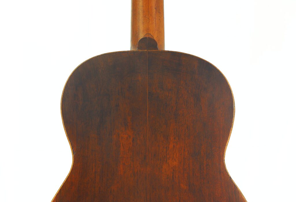 Nahaufnahme der Rückseite einer „Ricardo Sanchis Nacher 1940 Augustin Barrios Klassische Gitarre“, die die Holzstruktur und Maserung des Instruments zeigt, wobei der Hals nach oben verläuft und der Gitarrenkorpus eine satte braune Lackierung aufweist. Nahaufnahme der Rückseite einer „Ricardo Sanchis Nacher 1940 Augustin Barrios Klassische Gitarre“, die die Holzstruktur und Maserung des Instruments zeigt, wobei der Hals nach oben verläuft und der Gitarrenkorpus eine satte braune Lackierung aufweist.