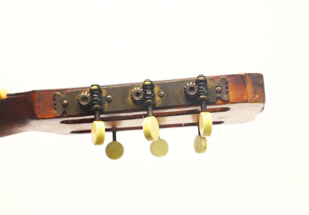 Nahaufnahme der Stimmwirbel und der Kopfplatte einer José Ramirez 1932 Klassische Gitarre, auf der die Metallzahnräder vor weißem Hintergrund zu sehen sind. Nahaufnahme der Stimmwirbel und der Kopfplatte einer José Ramirez 1932 Klassische Gitarre, auf der die Metallzahnräder vor weißem Hintergrund zu sehen sind.