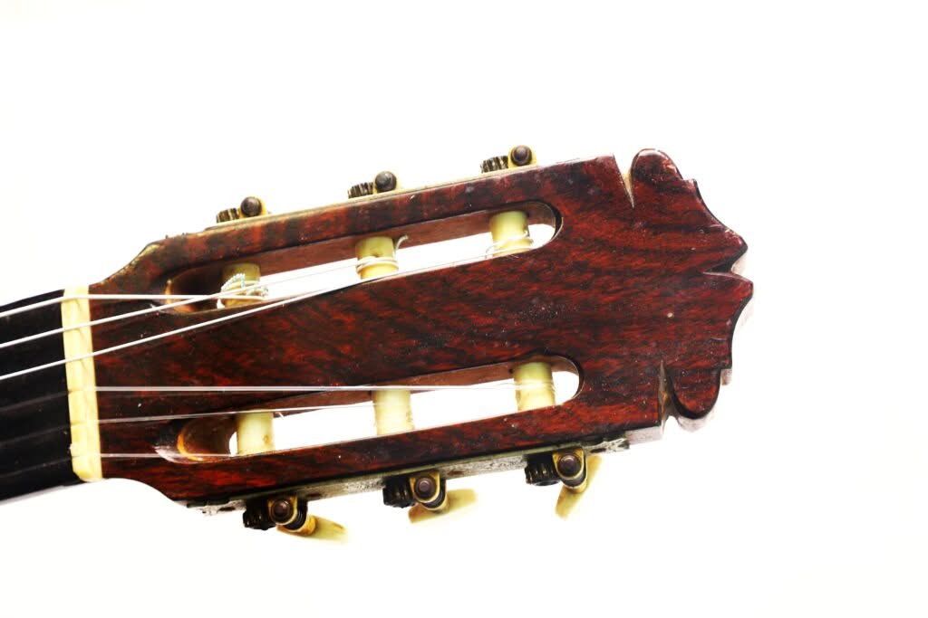 Nahaufnahme des Kopfes einer Flamenco-Gitarre von Manuel de la Chica aus dem Jahr 1954 mit Holzoberfläche, weißen Stimmwirbeln und Metallstimmmechaniken vor weißem Hintergrund. Nahaufnahme des Kopfes einer Flamenco-Gitarre von Manuel de la Chica aus dem Jahr 1954 mit Holzoberfläche, weißen Stimmwirbeln und Metallstimmmechaniken vor weißem Hintergrund.