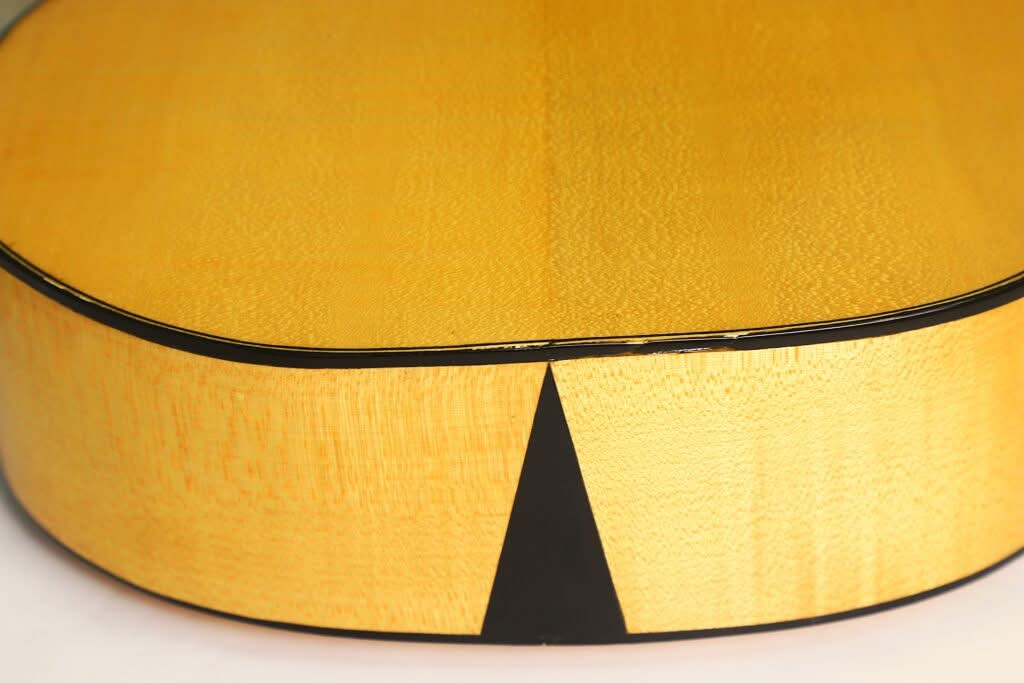 Nahaufnahme der Lacote Stil Romantikgitarre, die den Blick auf den glatten, hellen Holzboden und die Zargen, die schwarze Einfassung sowie die einzigartige schwarze dreieckige Einlage am unteren Rand lenkt. Nahaufnahme der Lacote Stil Romantikgitarre, die den Blick auf den glatten, hellen Holzboden und die Zargen, die schwarze Einfassung sowie die einzigartige schwarze dreieckige Einlage am unteren Rand lenkt.