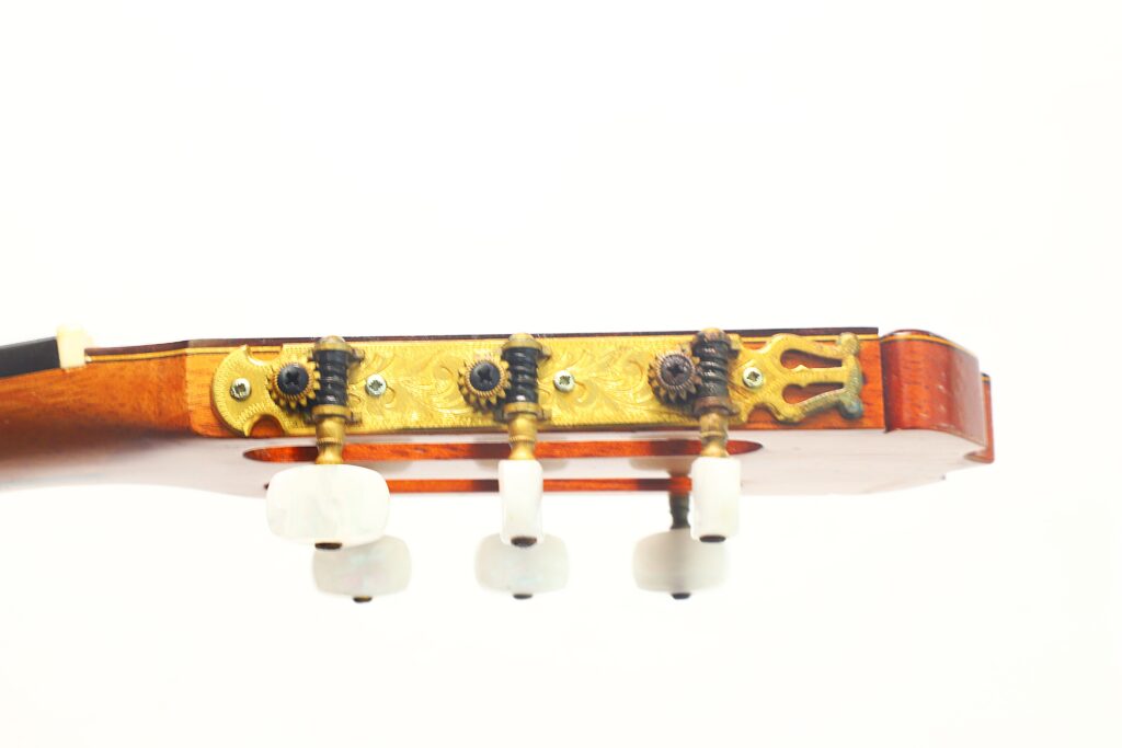 Nahaufnahme des Kopfes einer José Ramirez 1a 1973 Klassische Gitarre, die drei weiße Stimmwirbel, einen goldenen Stimmmechanismus und einen Teil des Holzhalses vor weißem Hintergrund zeigt. Nahaufnahme des Kopfes einer José Ramirez 1a 1973 Klassische Gitarre, die drei weiße Stimmwirbel, einen goldenen Stimmmechanismus und einen Teil des Holzhalses vor weißem Hintergrund zeigt.
