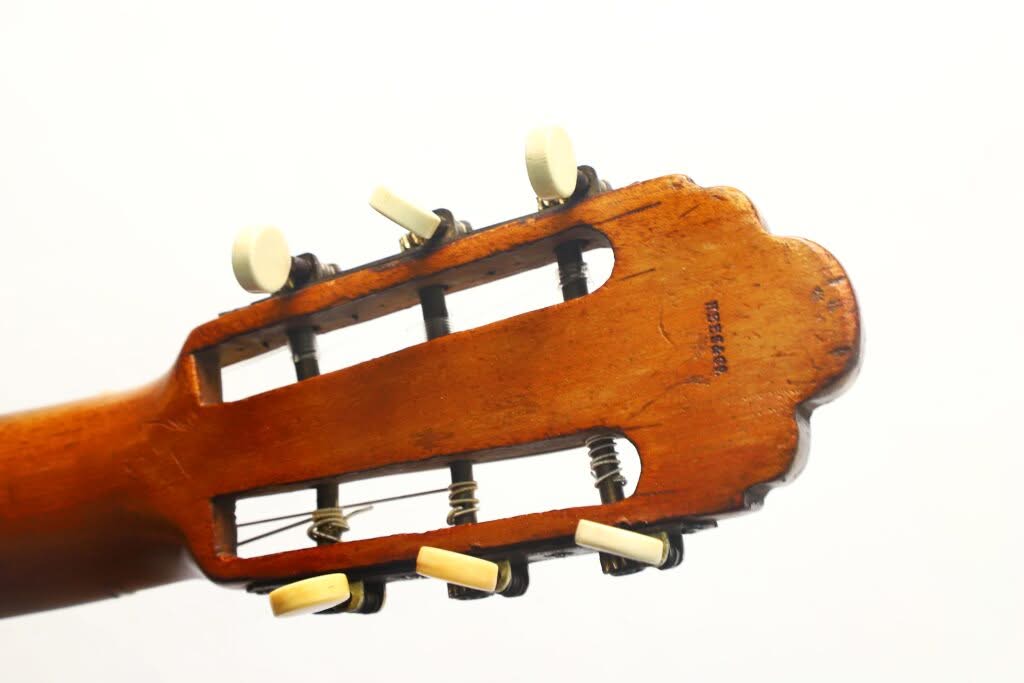 Nahaufnahme des Kopfes der „Salvador Ibanez 1900 Klassische Gitarre“ mit Stimmwirbeln und Saiten vor einem schlichten weißen Hintergrund. Das Holz weist eine warmbraune Lackierung mit gewellten Kanten auf. Nahaufnahme des Kopfes der „Salvador Ibanez 1900 Klassische Gitarre“ mit Stimmwirbeln und Saiten vor einem schlichten weißen Hintergrund. Das Holz weist eine warmbraune Lackierung mit gewellten Kanten auf.