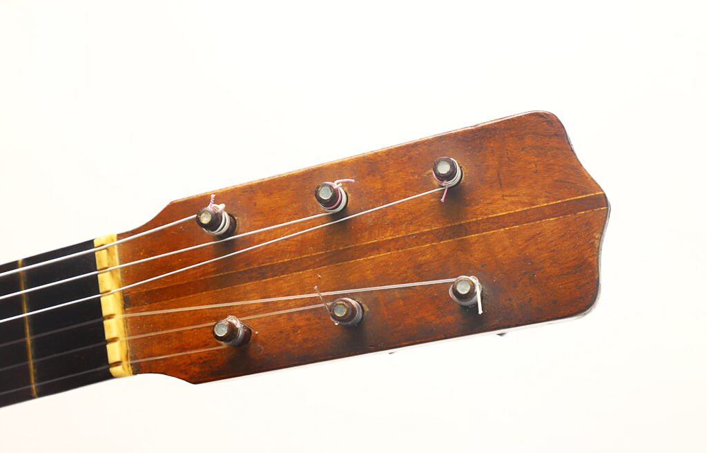 Nahaufnahme des Kopfes einer „Ricardo Sanchis Nacher 1940 Augustin Barrios Klassische Gitarre“ mit sechs Stimmwirbeln und Saiten vor einem schlichten weißen Hintergrund. Nahaufnahme des Kopfes einer „Ricardo Sanchis Nacher 1940 Augustin Barrios Klassische Gitarre“ mit sechs Stimmwirbeln und Saiten vor einem schlichten weißen Hintergrund.