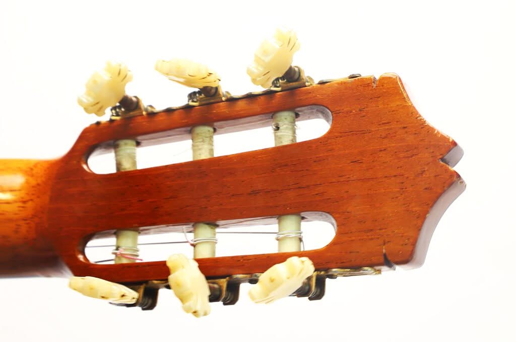Nahaufnahme des Kopfes einer Flamenco-Gitarre von Sobrinos de Santos Hernandez aus dem Jahr 1974, mit sechs weißen Stimmwirbeln und Nylonsaiten vor einem schlichten weißen Hintergrund. Nahaufnahme des Kopfes einer Flamenco-Gitarre von Sobrinos de Santos Hernandez aus dem Jahr 1974, mit sechs weißen Stimmwirbeln und Nylonsaiten vor einem schlichten weißen Hintergrund.