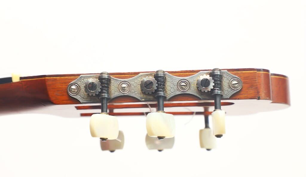 Nahaufnahme der Kopfplatte der „Hauser Klassische Gitarre“ von Alastair McNeil aus dem Jahr 1997 in Seitenansicht, auf der die Stimmwirbel, die Zahnräder und ein Teil des Holzhalses vor weißem Hintergrund zu sehen sind. Nahaufnahme der Kopfplatte der „Hauser Klassische Gitarre“ von Alastair McNeil aus dem Jahr 1997 in Seitenansicht, auf der die Stimmwirbel, die Zahnräder und ein Teil des Holzhalses vor weißem Hintergrund zu sehen sind.