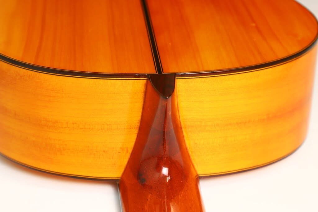 Nahaufnahme der Rückseite einer Flamenco-Gitarre von Sobrinos de Santos Hernandez aus dem Jahr 1974, die den glänzenden Holzlack, den Halsansatz und die Nahtstelle zwischen den beiden Hälften des Gitarrenkorpus hervorhebt. Nahaufnahme der Rückseite einer Flamenco-Gitarre von Sobrinos de Santos Hernandez aus dem Jahr 1974, die den glänzenden Holzlack, den Halsansatz und die Nahtstelle zwischen den beiden Hälften des Gitarrenkorpus hervorhebt.