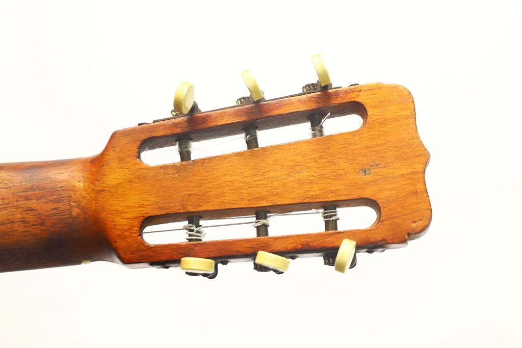 Nahaufnahme der Rückseite des Kopfes einer José Ramirez „Klassische Gitarre“ von 1932 mit cremefarbenen Stimmwirbeln und sichtbaren Stimmmechanismen vor einem schlichten weißen Hintergrund. Nahaufnahme der Rückseite des Kopfes einer José Ramirez „Klassische Gitarre“ von 1932 mit cremefarbenen Stimmwirbeln und sichtbaren Stimmmechanismen vor einem schlichten weißen Hintergrund.