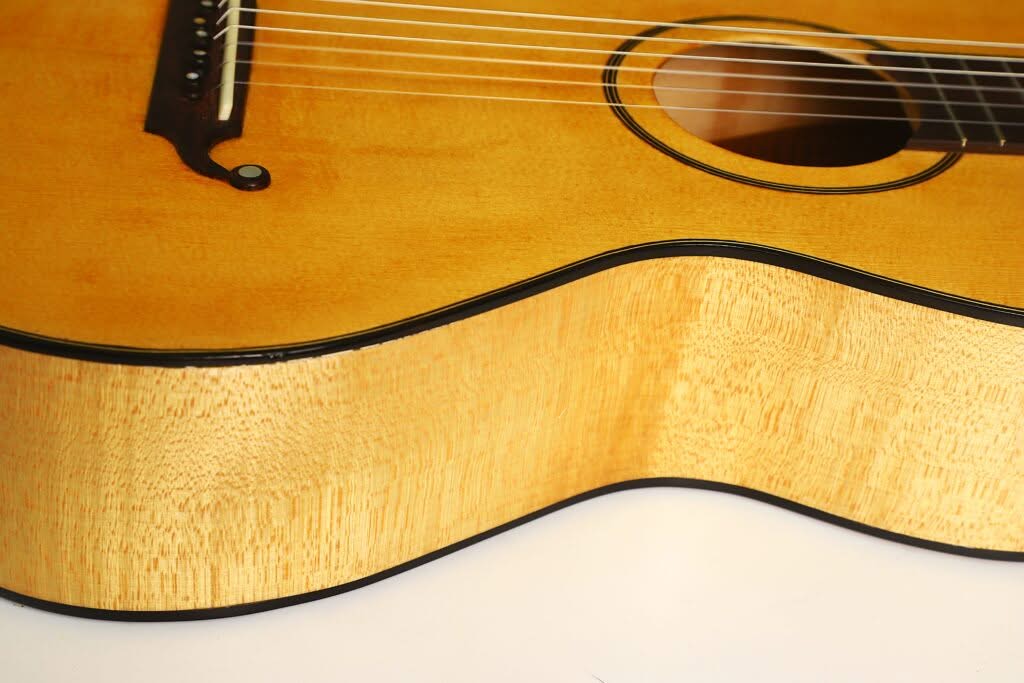Nahaufnahme des Korpus der Lacote Stil Romantikgitarre mit heller Holzmaserung, schwarzer Zierleiste, Saiten und einem Teil des Schalllochs, fotografiert vor weißem Hintergrund. Nahaufnahme des Korpus der Lacote Stil Romantikgitarre mit heller Holzmaserung, schwarzer Zierleiste, Saiten und einem Teil des Schalllochs, fotografiert vor weißem Hintergrund.