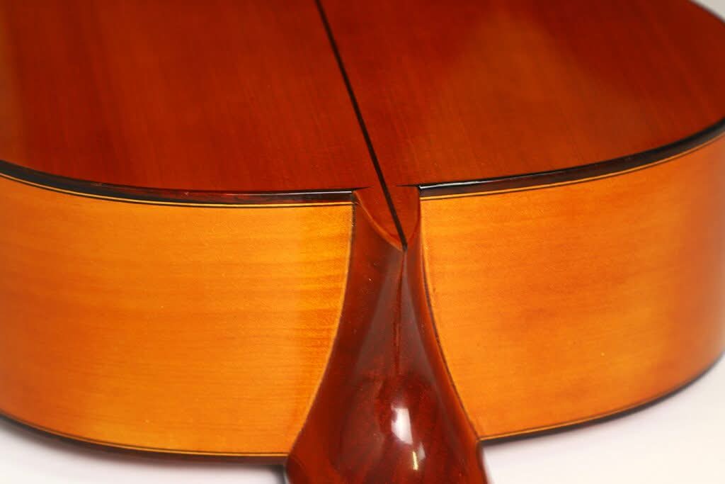Nahaufnahme der Rückseite einer Jose Ramirez 1a Flamenco-Gitarre aus dem Jahr 1968, mit Fokus auf den geschwungenen Bereich, an dem der Hals in den Korpus übergeht, wobei die Holzmaserung und die glänzende Lackierung besonders hervorgehoben werden. Nahaufnahme der Rückseite einer Jose Ramirez 1a Flamenco-Gitarre aus dem Jahr 1968, mit Fokus auf den geschwungenen Bereich, an dem der Hals in den Korpus übergeht, wobei die Holzmaserung und die glänzende Lackierung besonders hervorgehoben werden.