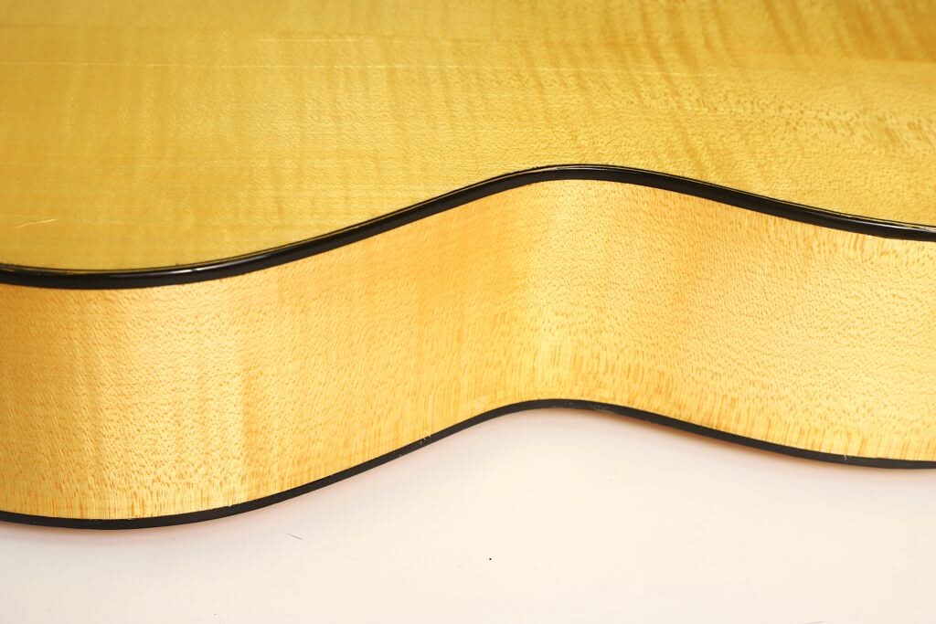 Nahaufnahme der hellen Holzseite und der geschwungenen Kante der Akustikgitarre „Lacote Stil Romantikgitarre“, die die glatte Oberfläche und die schwarze Einfassung zeigt. Nahaufnahme der hellen Holzseite und der geschwungenen Kante der Akustikgitarre „Lacote Stil Romantikgitarre“, die die glatte Oberfläche und die schwarze Einfassung zeigt.