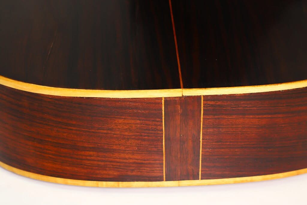 Nahaufnahme der Rückseite und der Seite der „Salvador Ibanez 1900 Klassische Gitarre“, die die dunkle Holzmaserung, die vertikale Einlage in der Mitte und die helle Einfassung entlang des Korpus hervorhebt. Nahaufnahme der Rückseite und der Seite der „Salvador Ibanez 1900 Klassische Gitarre“, die die dunkle Holzmaserung, die vertikale Einlage in der Mitte und die helle Einfassung entlang des Korpus hervorhebt.
