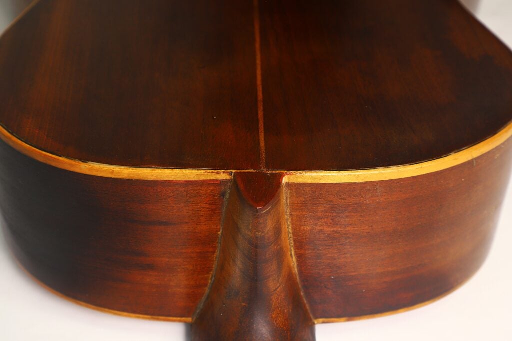 Nahaufnahme der Rückseite einer „José Ramirez 1932 Klassische Gitarre“, die vor einem neutralen Hintergrund die elegante Holzmaserung, den Halsansatz und eine gelbliche Einfassung entlang der Korpuskanten hervorhebt. Nahaufnahme der Rückseite einer „José Ramirez 1932 Klassische Gitarre“, die vor einem neutralen Hintergrund die elegante Holzmaserung, den Halsansatz und eine gelbliche Einfassung entlang der Korpuskanten hervorhebt.