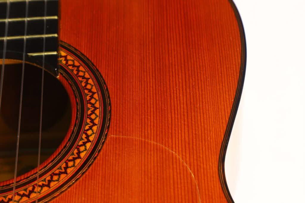 Nahaufnahme der Flamenco-Gitarre „Jose Ramirez 1a 1968“ mit Fokus auf den Korpus, die Saiten, die Zierrosette um das Schallloch sowie einen Ausschnitt der Holzoberfläche vor weißem Hintergrund. Nahaufnahme der Flamenco-Gitarre „Jose Ramirez 1a 1968“ mit Fokus auf den Korpus, die Saiten, die Zierrosette um das Schallloch sowie einen Ausschnitt der Holzoberfläche vor weißem Hintergrund.