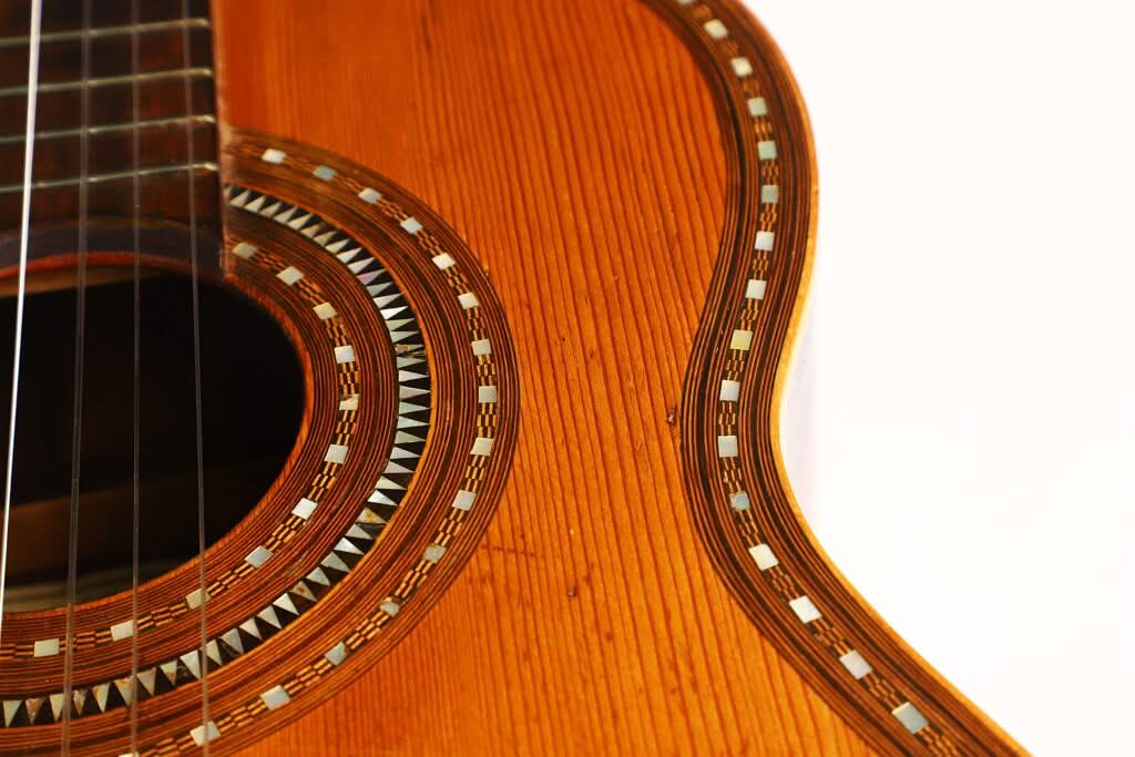 Nahaufnahme der „Salvador Ibanez 1900 Klassische Gitarre“, die die feine Holzmaserung, die Zierintarsien um das Schallloch sowie einen Teil der Saiten und des Korpus vor weißem Hintergrund hervorhebt. Nahaufnahme der „Salvador Ibanez 1900 Klassische Gitarre“, die die feine Holzmaserung, die Zierintarsien um das Schallloch sowie einen Teil der Saiten und des Korpus vor weißem Hintergrund hervorhebt.
