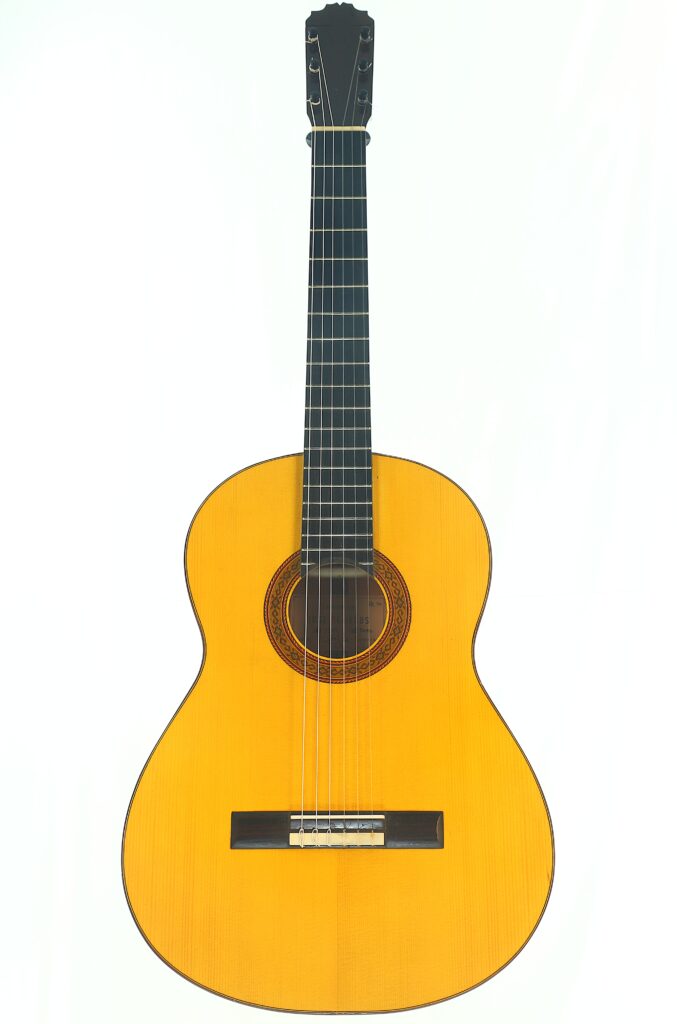 Eine Gesamtansicht der Jose de Jesus 2024 Blanca Modell Reyes Flamenco-Gitarre mit einem hellen Holzkorpus, einem dunklen Griffbrett und einem aufwendigen Rosettenmuster um das Schallloch herum, vor einem weißen Hintergrund. Eine Gesamtansicht der Jose de Jesus 2024 Blanca Modell Reyes Flamenco-Gitarre mit einem hellen Holzkorpus, einem dunklen Griffbrett und einem aufwendigen Rosettenmuster um das Schallloch herum, vor einem weißen Hintergrund.