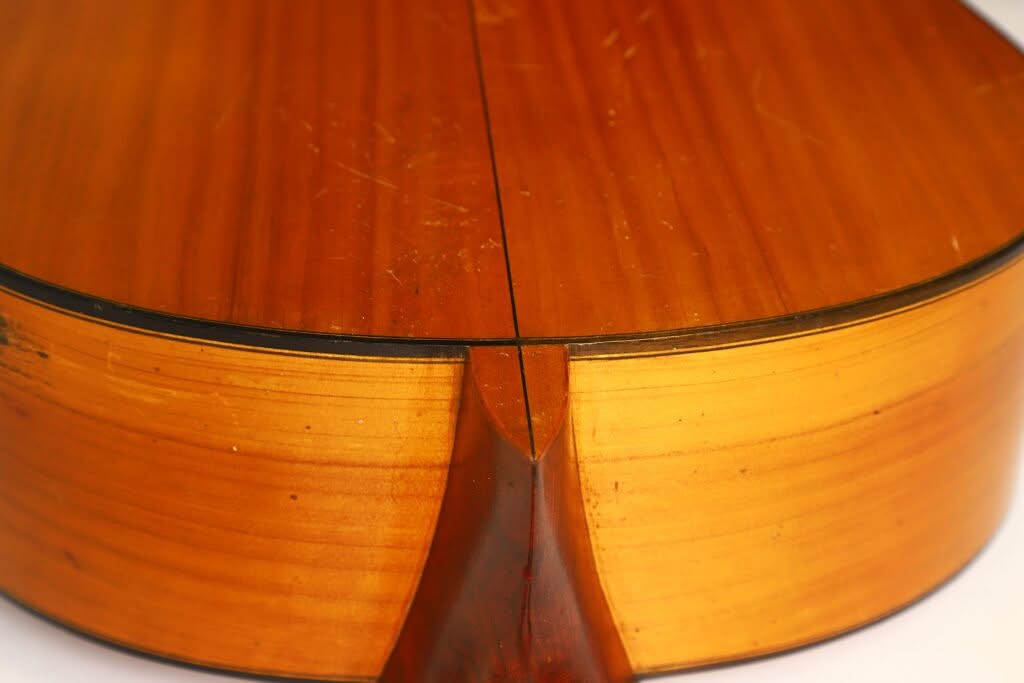 Nahaufnahme der Rückseite und der Zargen einer Flamenco-Gitarre von Manuel de la Chica aus dem Jahr 1954, bei der die Maserung des Holzes, die Mittellinie und der Halsfuß, an dem der Hals mit dem Korpus verbunden ist, besonders hervorgehoben werden. Nahaufnahme der Rückseite und der Zargen einer Flamenco-Gitarre von Manuel de la Chica aus dem Jahr 1954, bei der die Maserung des Holzes, die Mittellinie und der Halsfuß, an dem der Hals mit dem Korpus verbunden ist, besonders hervorgehoben werden.